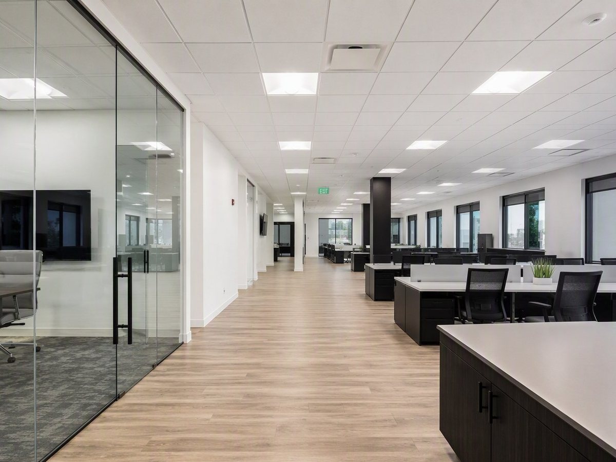 Finished commercial office floor with open workstations, glass-walled meeting rooms, and an LED panel ceiling
