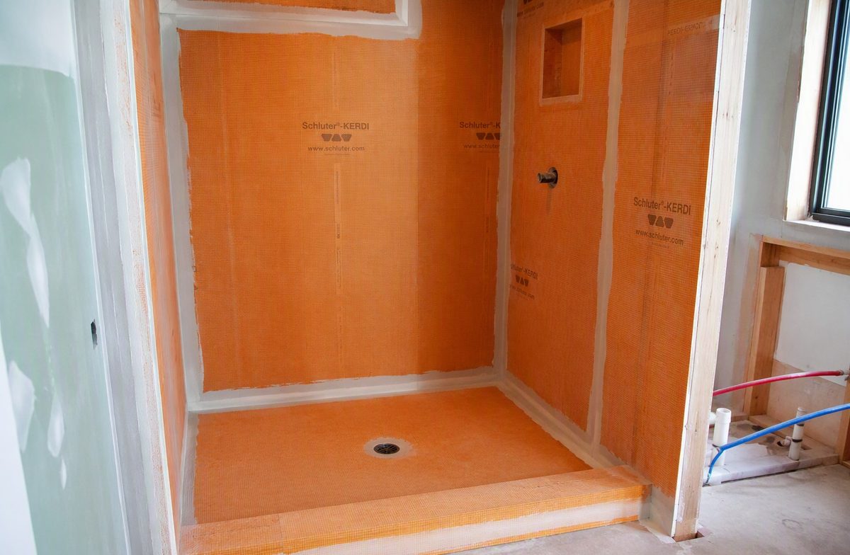 Shower walls and pan fully covered in orange waterproofing membrane, ready for tile